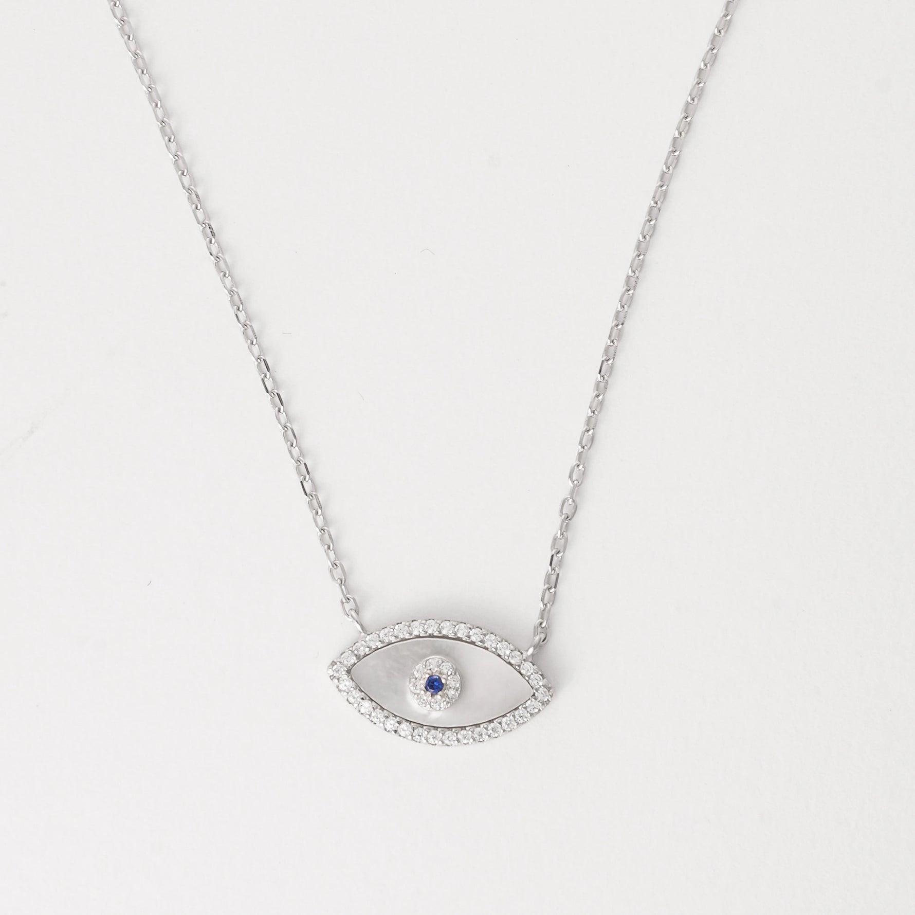 The Blue Center Evil Eye Necklace is crafted from fine silver, featuring a delicate eye design with a shimmering blue center surrounded by bright zircon stones.
