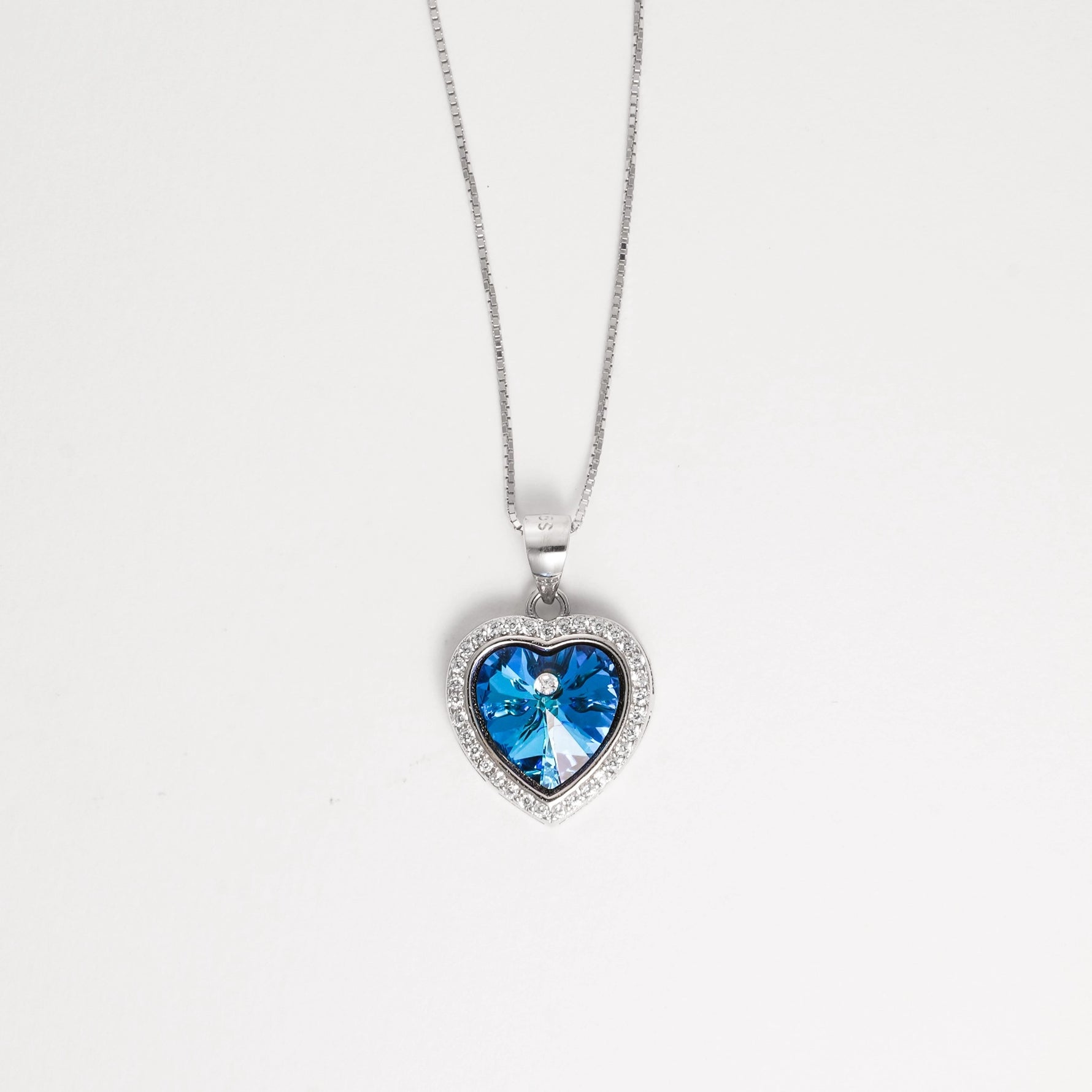 The Blue Heart Crystal Necklace is a stunning fine silver piece that captures the essence of elegance. At its center shines a brilliant blue heart-shaped crystal, surrounded by sparkling zircon stones that add a radiant glow.