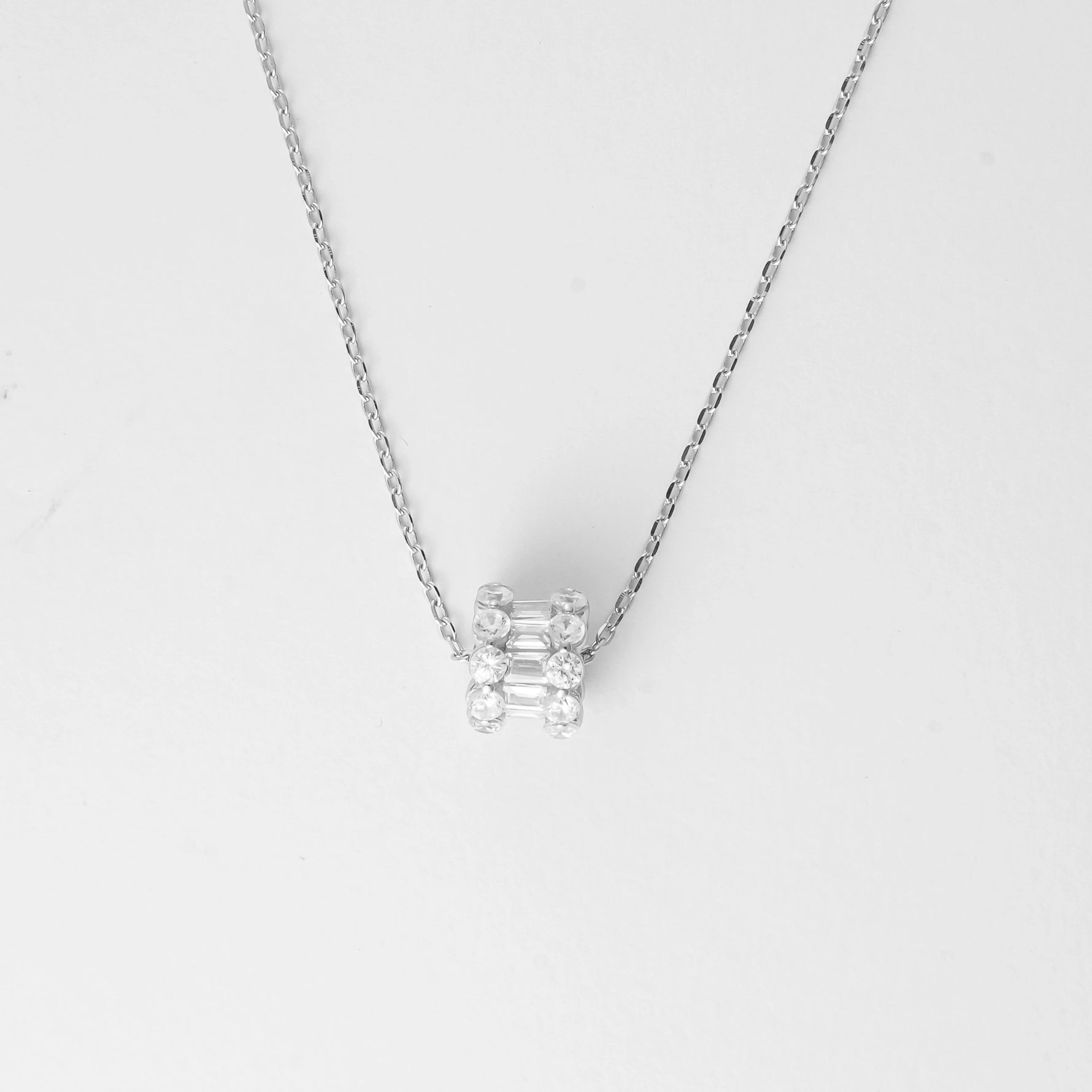 The Crystal Cylinder Necklace is a sleek and modern piece crafted from fine silver, adorned with dazzling bright zircon stones arranged in a unique cylindrical design. Its clean lines and sparkling details make it a versatile accessory that effortlessly elevates any outfit.