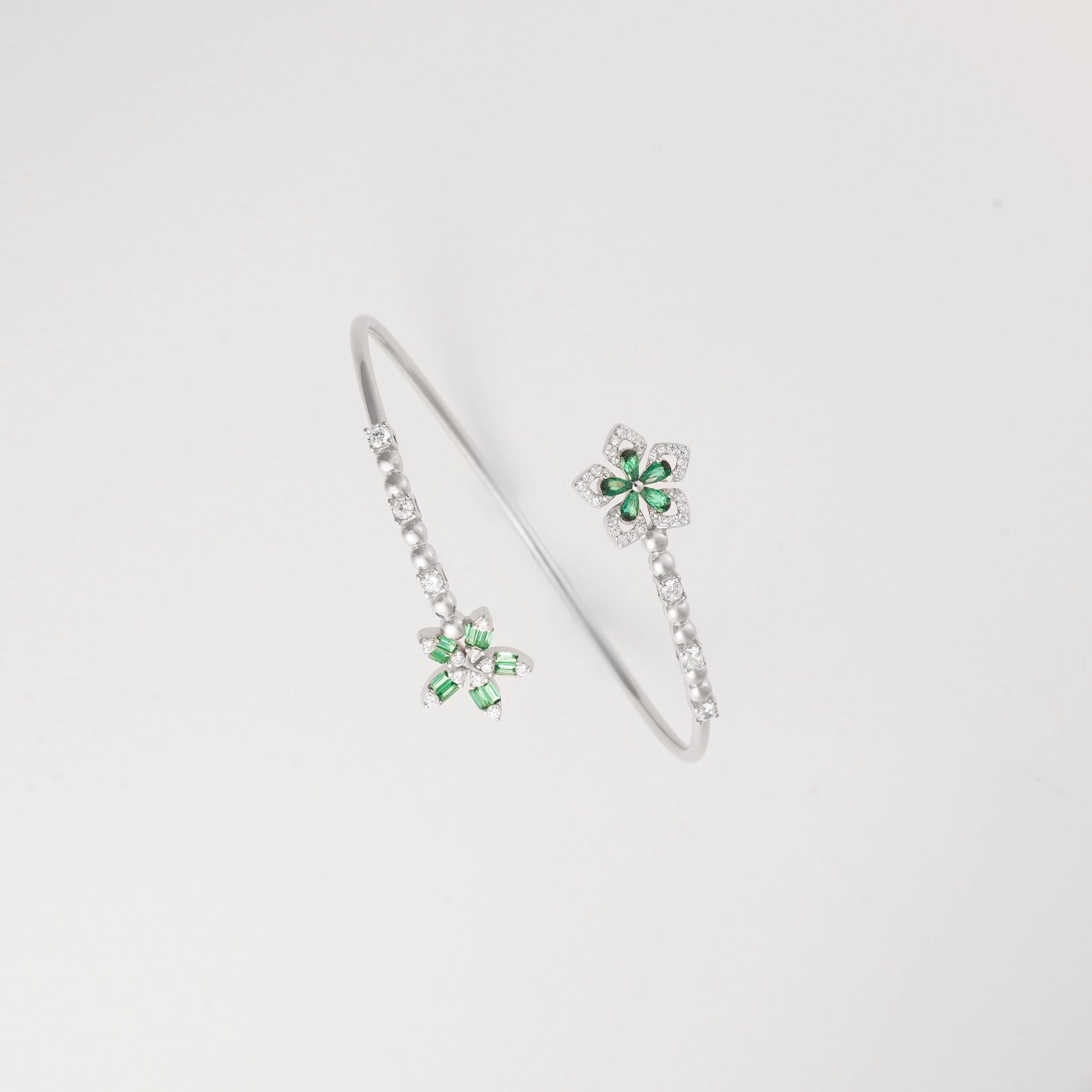 The Green Aura Bangle captures the essence of elegance with its twin floral designs, set in vivid emerald-toned stones and framed by radiant zircon accents.