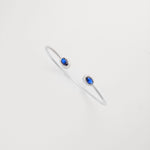 This sleek silver bangle features twin deep blue crystal stones, each framed by a delicate halo of white shining crystals.