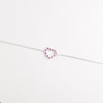 The Pink Gem Heart Bracelet showcases a delicate open-heart charm set with bright pink zircon stones and tiny crystals.