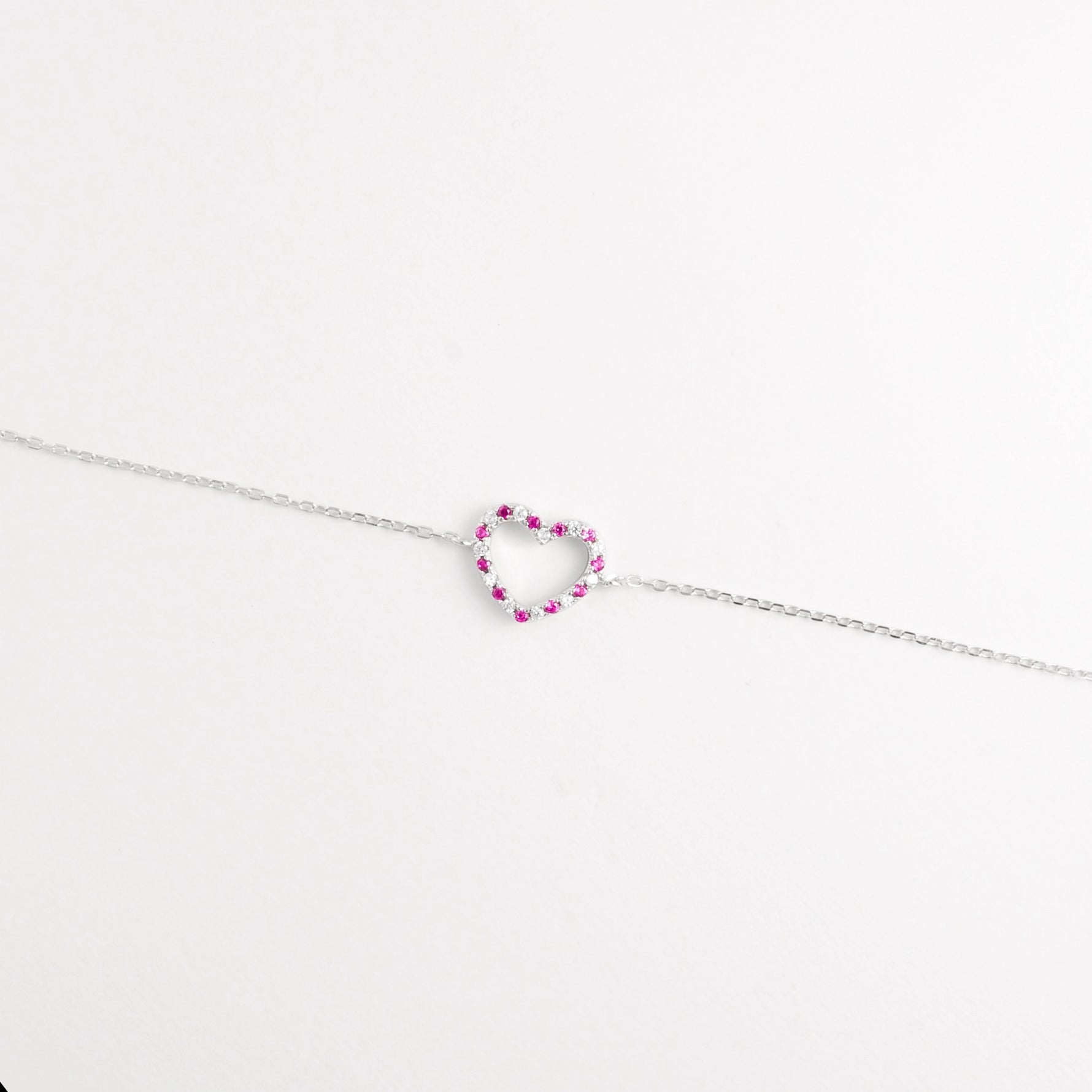 The Pink Gem Heart Bracelet showcases a delicate open-heart charm set with bright pink zircon stones and tiny crystals.