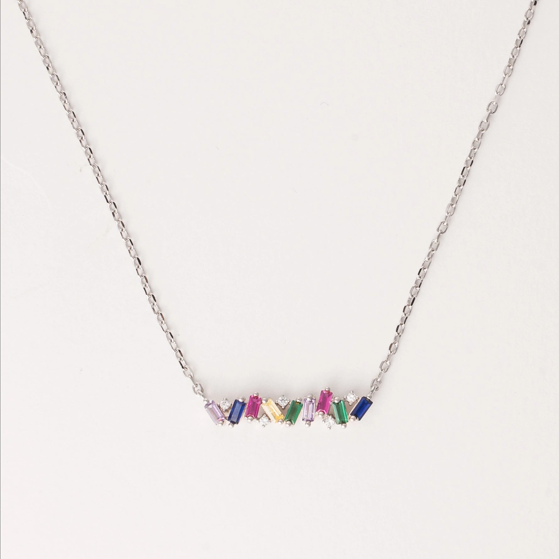 The Rainbow Gem Bar Necklace is a vibrant and elegant piece made from fine silver, featuring a row of dazzling zircon stones in a spectrum of colors.