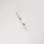 This open silver bangle is accented with a deep blue crystal on one end and a shimmering clear crystal cluster on the other.