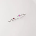 Simple, stylish, and full of charm. This open silver bangle is accented with a deep red crystal on one end and a shimmering clear crystal cluster on the other.