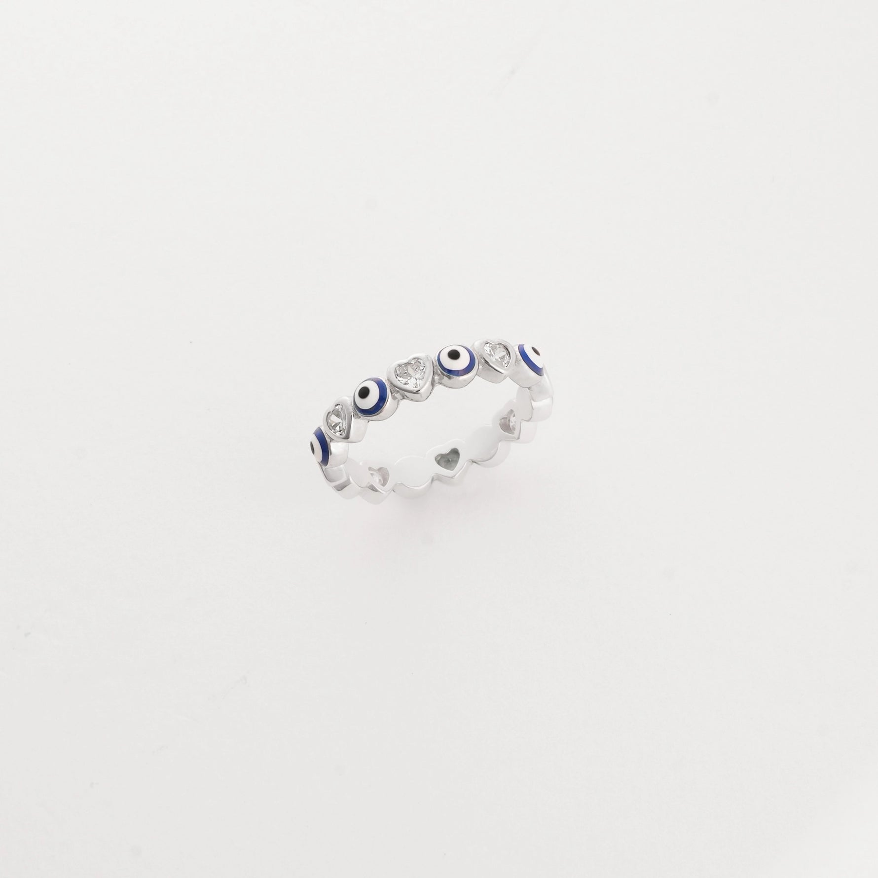 The Evil Eye Charm ring features a sleek silver band decorated with a playful pattern of blue evil eye motifs and bright stones.