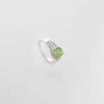 The Emerald Aura ring showcases a striking round green gemstone, secured in a sleek silver setting. Bright zircon stones line the split band, adding shimmer and balance.