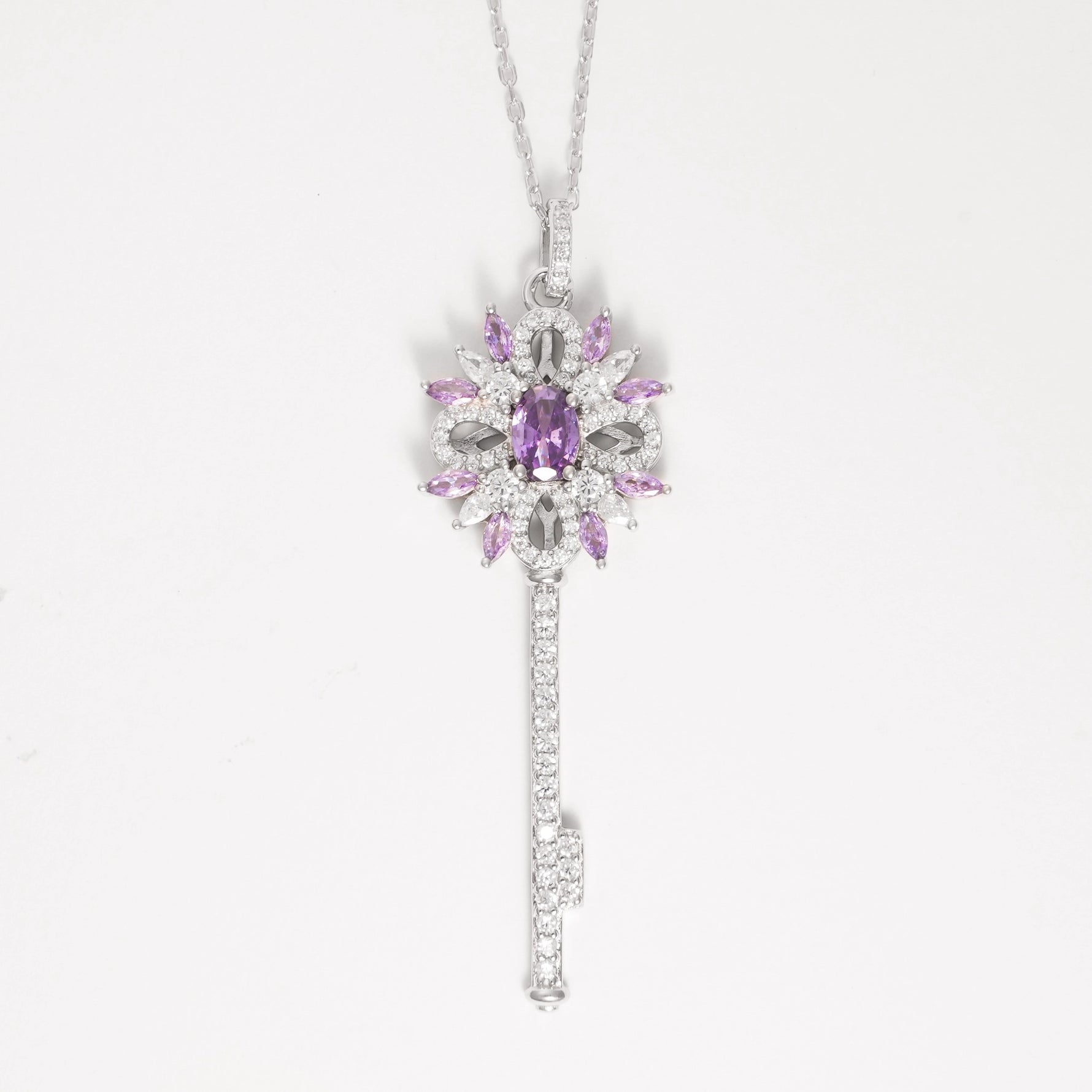 The Key to Elegance Necklace is a beautifully crafted piece in fine silver, featuring a delicate key pendant adorned with shimmering zircon stones and sparkling purple crystals.