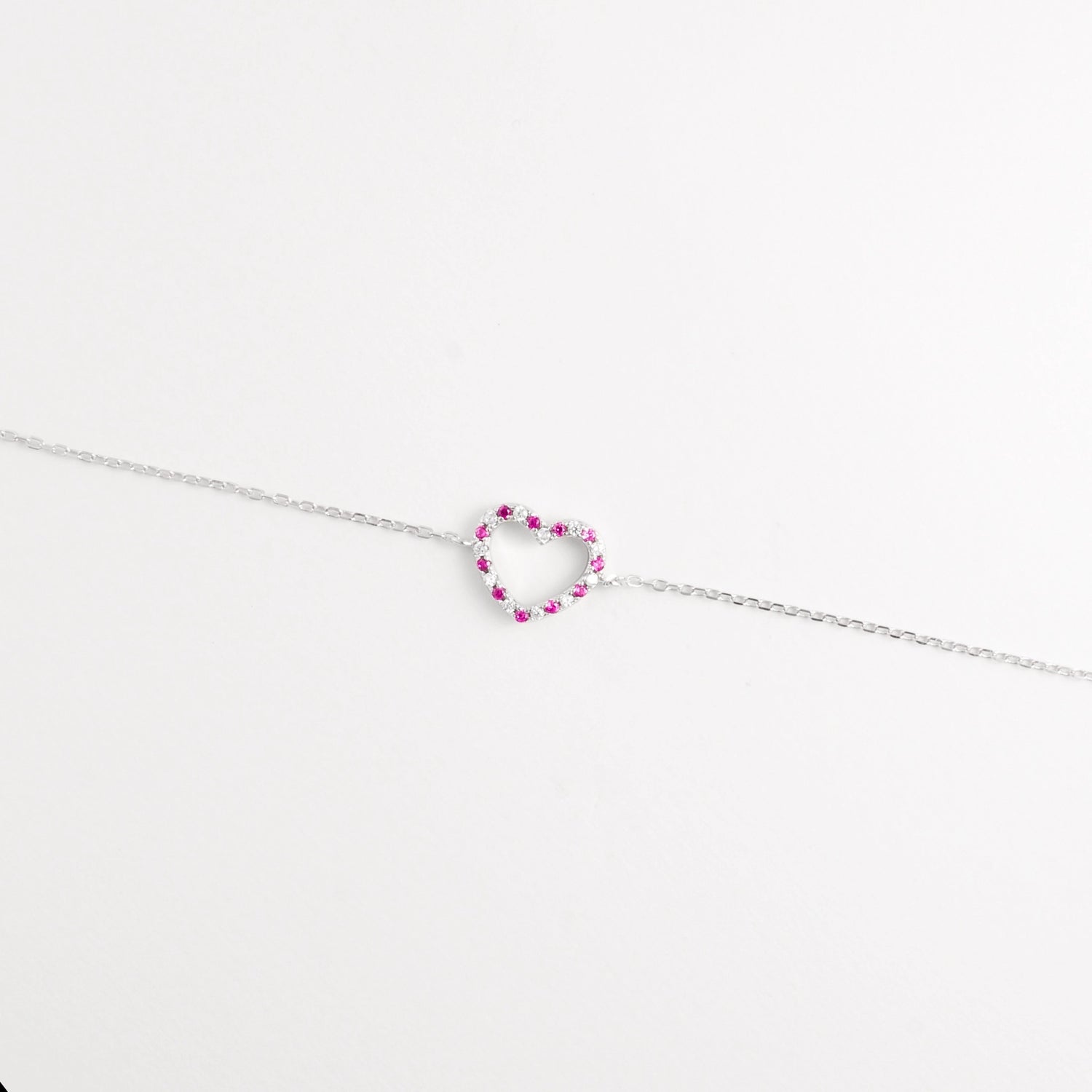 The Pink Gem Heart Bracelet showcases a delicate open-heart charm set with bright pink zircon stones and tiny crystals.