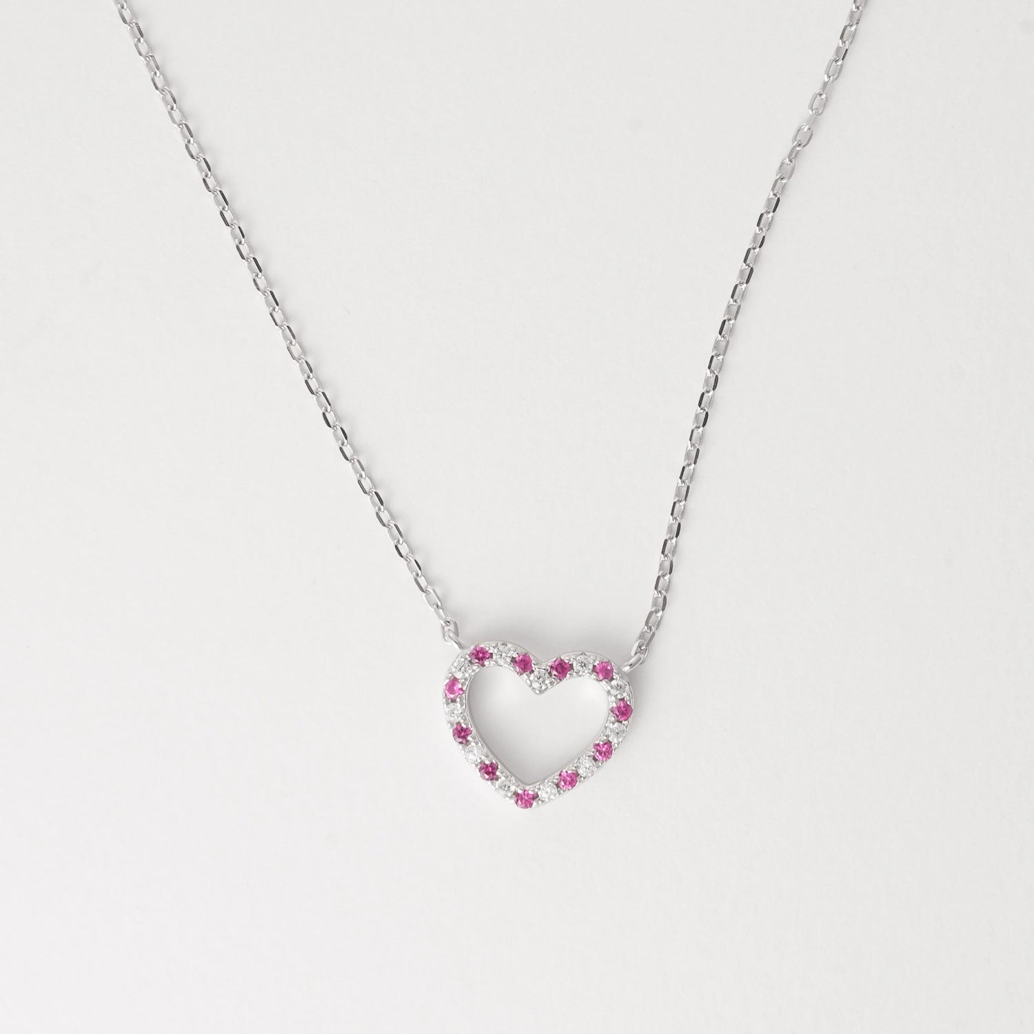 Sweet, minimal, and full of charm the Pink Heart Outline Necklace is crafted from fine silver and set with alternating bright pink and white zircon stones that delicately outline its open-heart shape. 