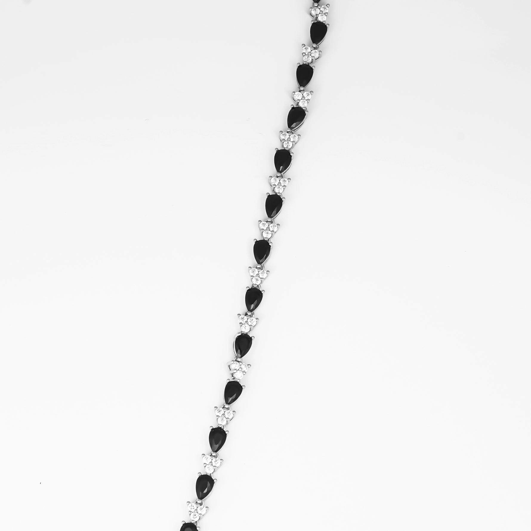 the Teardrop Black Tennis Bracelet, a stunning accessory crafted from fine silver and adorned with sparkling zircon stones. The unique teardrop-shaped black zircon stones alternate with bright clear zircons, creating a chic and elegant look.