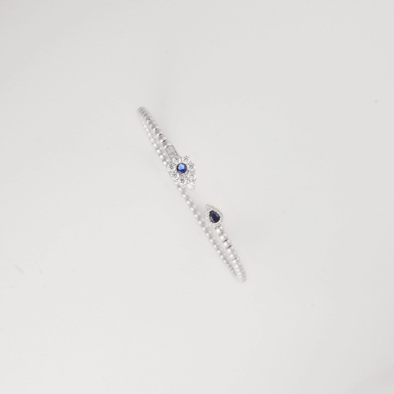 This open silver bangle is accented with a deep blue crystal on one end and a shimmering clear crystal cluster on the other.