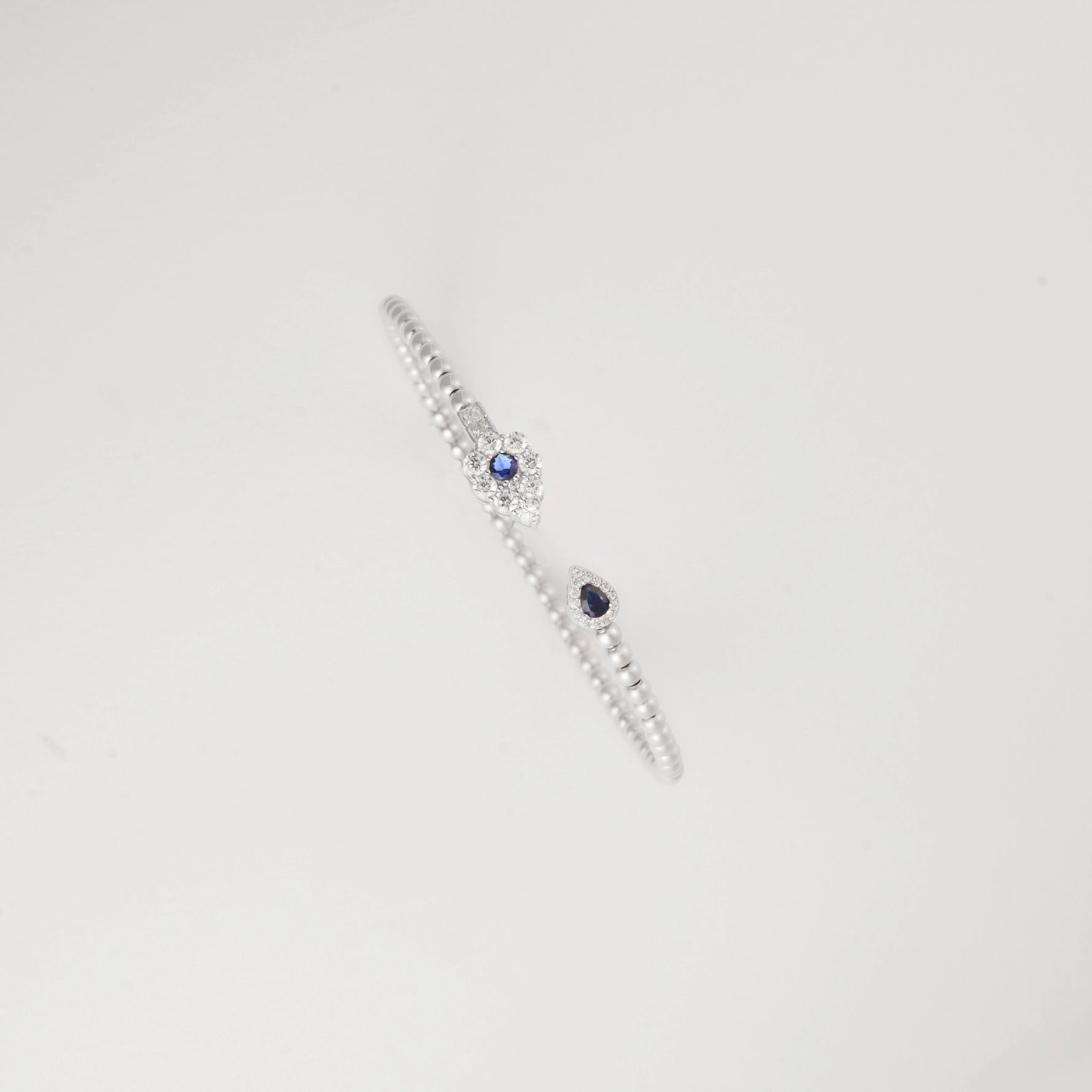 This open silver bangle is accented with a deep blue crystal on one end and a shimmering clear crystal cluster on the other.