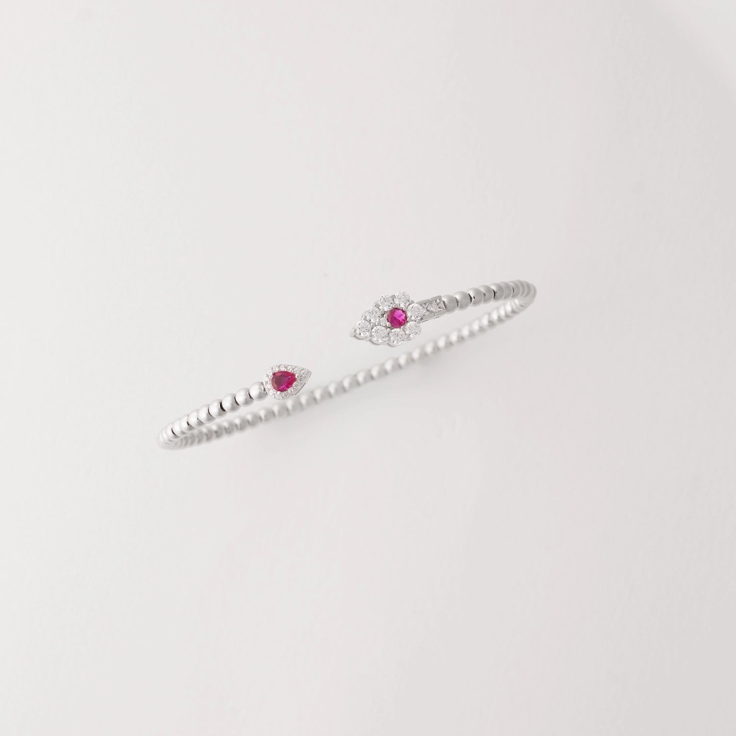 Simple, stylish, and full of charm. This open silver bangle is accented with a deep red crystal on one end and a shimmering clear crystal cluster on the other.