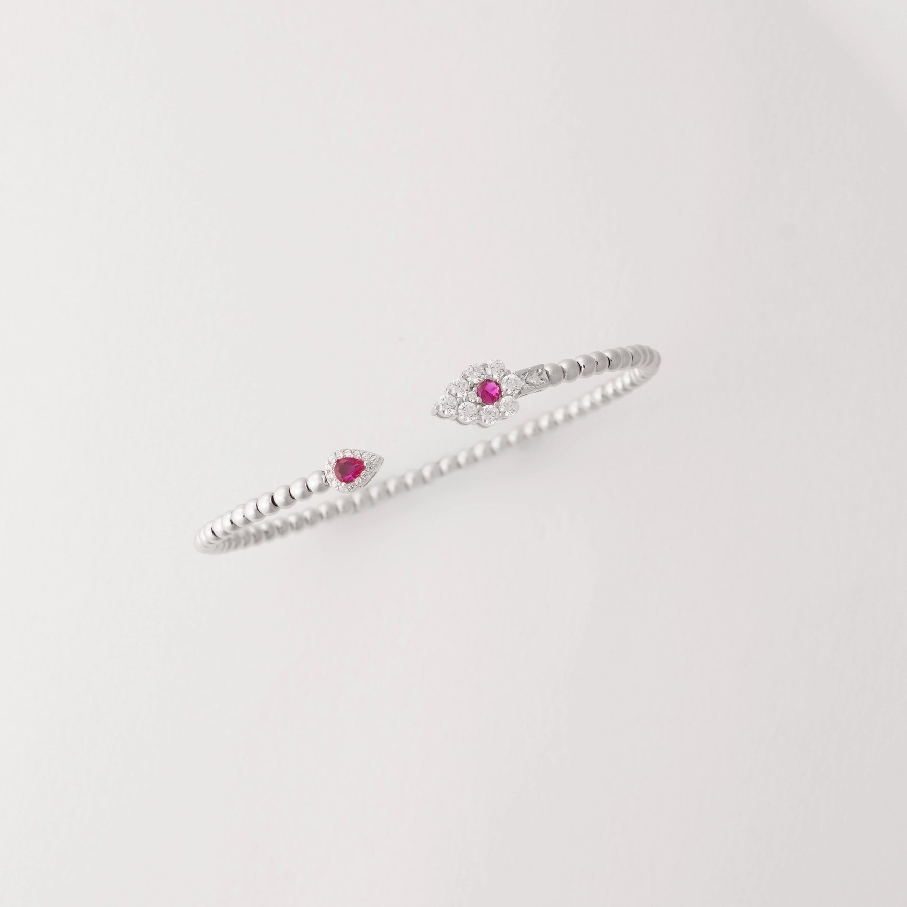 Simple, stylish, and full of charm. This open silver bangle is accented with a deep red crystal on one end and a shimmering clear crystal cluster on the other.